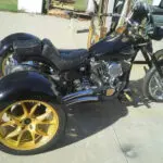 A black motorcycle with yellow wheels parked on the sidewalk.