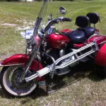 A red motorcycle with a side car parked in the grass.