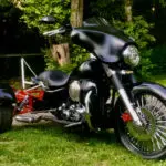 A black motorcycle parked in the grass near trees.