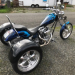 A blue and black three wheeled motorcycle parked on the street.