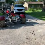 A red and silver three wheeled motorcycle parked on the side of a road.