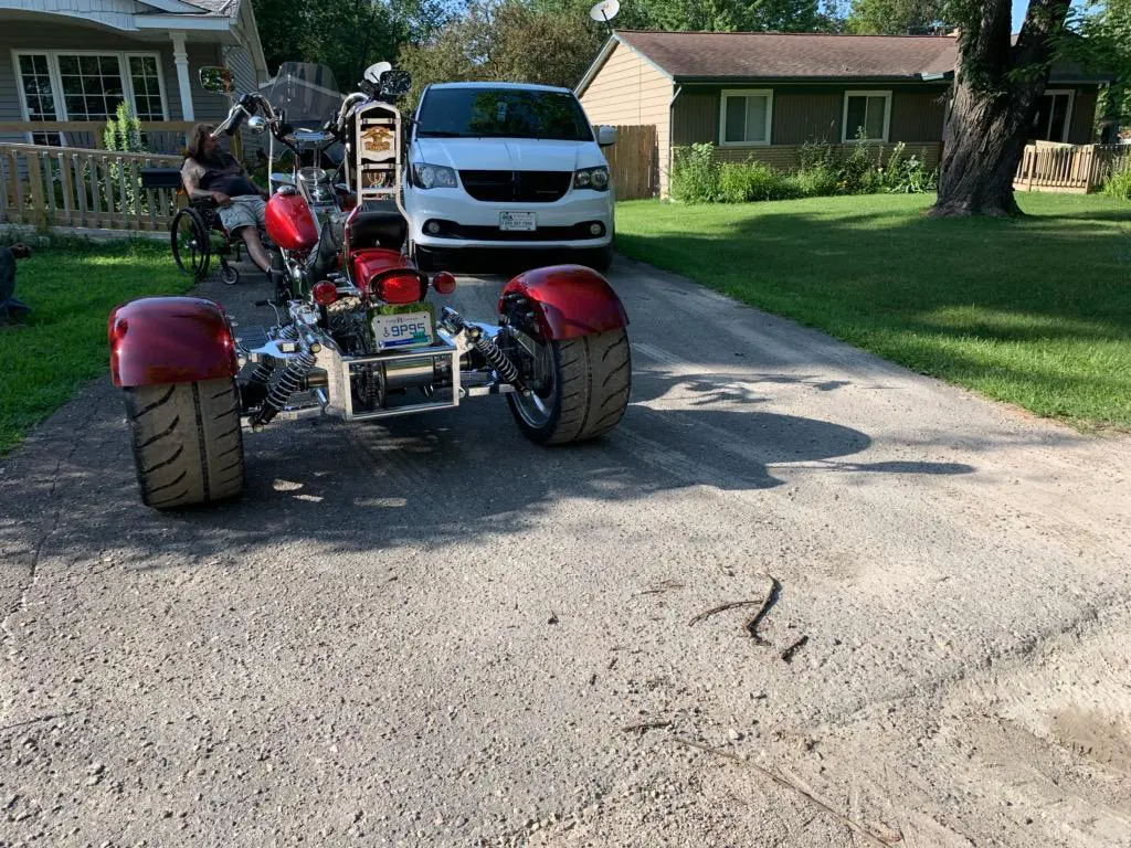 A red and silver three wheeled motorcycle parked on the side of a road.