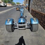 A blue three wheeled motorcycle parked on the side of a street.