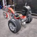 A red and orange three wheeled motorcycle parked on the side of road.