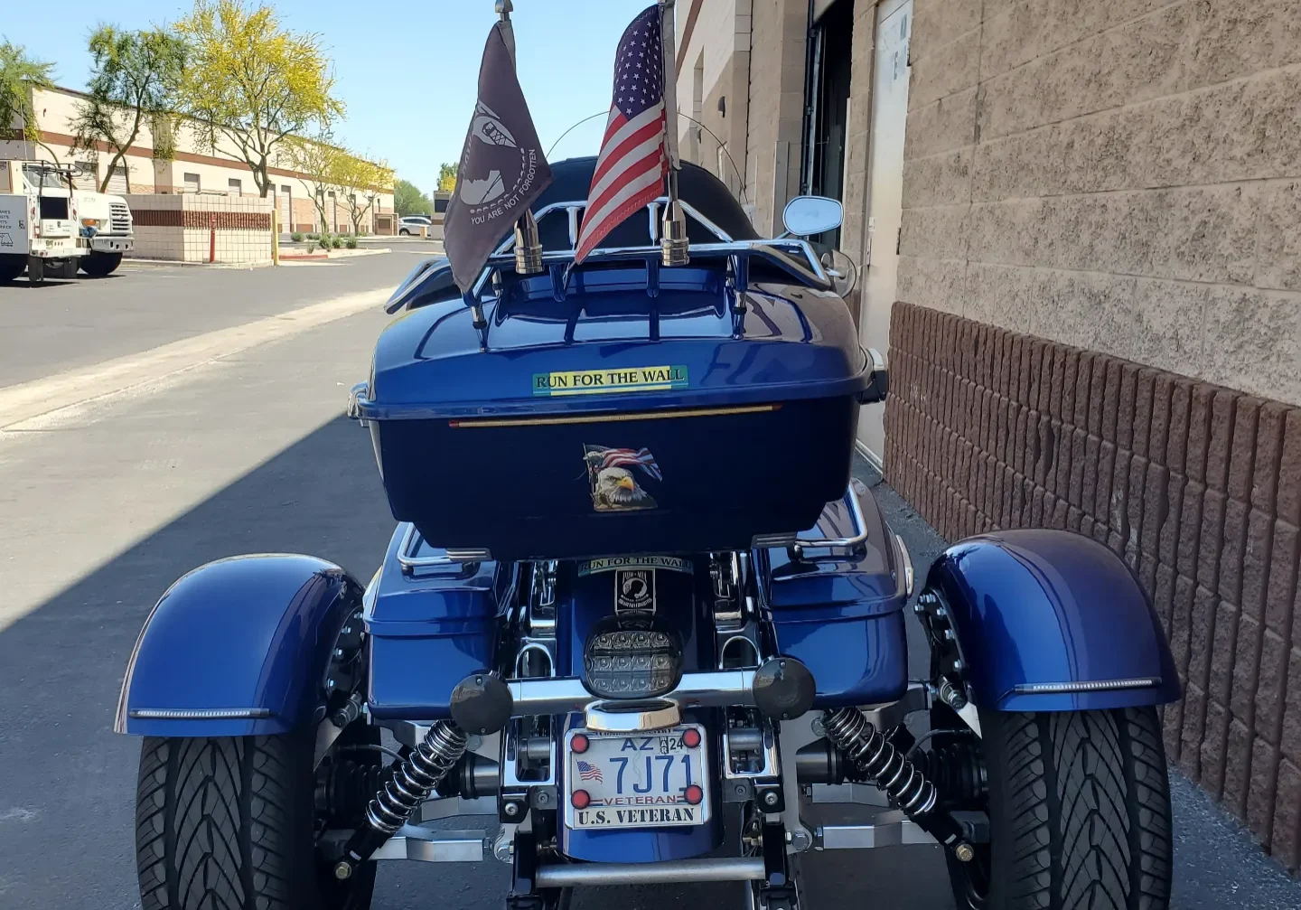 A blue three wheeled motorcycle parked on the side of a street.